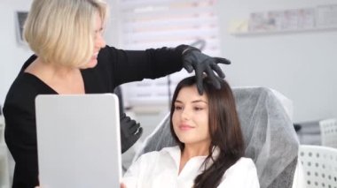 A beautiful young brunette with the masters eyebrows. A cosmetologist prepares a woman for the procedure of permanent eyebrow makeup. Beauty salon.
