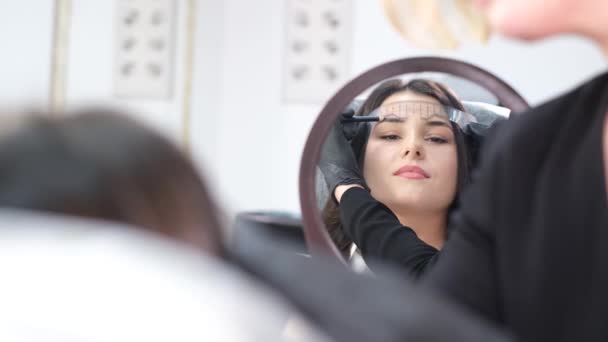 永久的な眉メイクの手順の準備 鏡の前の美容室で美しい若い女性 眉の輪郭 — ストック動画