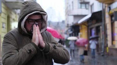 Genç bir adamın burnu akıyor. Viral grip enfeksiyonu. Şehrin ortasında üşütmüş genç bir adam..