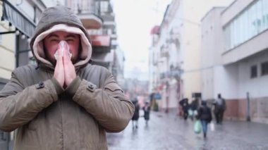 A young man with a cold in the middle of a city street. Runny nose during the flu. Viral infections.