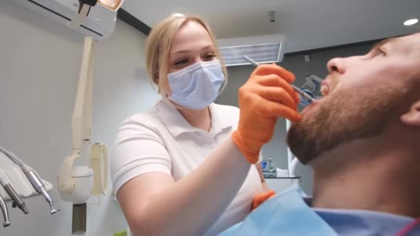 歯医者は歯医者の椅子に座っている若い男の歯を調べる 歯の配置 インプラントの設置 — ストック動画