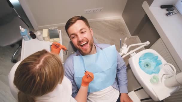 一名女牙医检查坐在牙椅上的一名年轻男子的牙齿 牙科学 牙齿的对齐 安装假牙植入物 — 图库视频影像