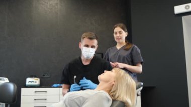 A dentist and an assistant during an examination of an elderly woman sitting in a dental chair. Painless dental treatment. 4k video
