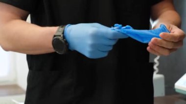 The dentist puts on sterile rubber gloves before examining the patient. Doctors hands close-up.