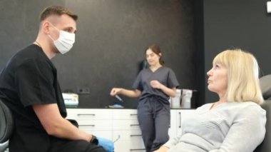An elderly woman is sitting in a dental office and talking to a doctor. A retired woman undergoing dental treatment. Installation of dental implants for the elderly