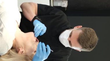 Vertical video, a dentist treats the teeth of a beautiful elderly woman. A retired woman at a dentists appointment. Installation of dental implants for the elderly