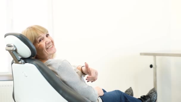 シニア女性歯科椅子に座って親指を表示します 年金受給者は歯科治療に満足しています 年上の女性の美しい笑顔 — ストック動画