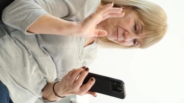 ヨーロッパ人の引退した女性は 現代的なスマートフォンを使用してインターネット上で話します 高齢者は現代のガジェットを使用します 垂直ビデオ — ストック動画
