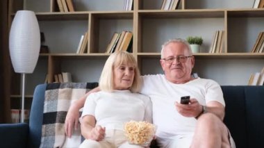 Senior couple watching television and eating popcorn at home. Enjoying leisure time. Happy family concept.