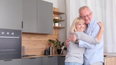 Senior couple dancing together in the kitchen, smiling. Retirement and happy senior living concept.Couple in the kitchen at home.