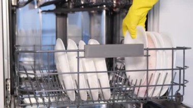 A womans hands load dirty dishes into a dishwasher, an open door reveals a built-in dishwasher, and dishes are loaded with dishwashing capsules. 