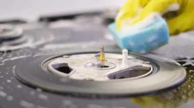 A woman cleans a gas stove in the kitchen with a sponge with washing-up liquid. House cleaning services