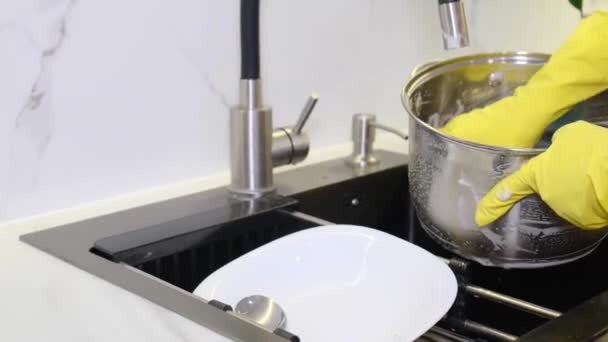 ゴム手袋とスポンジを身に着けている金属鍋を洗う女性のクローズアップ 女性は徐々に水で鍋を洗います キッチンのきれいな料理 — ストック動画