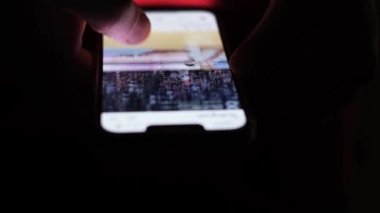 Man looks at his mobile phone at night, browsing through social networks close-up, while touching his fingers on the mobile phone while chatting indoors. Life in a mobile application.