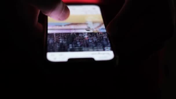男は夜に携帯電話を見て 屋内でチャットしながら携帯電話に指を触れながら ソーシャルネットワークのクローズアップを閲覧します モバイルアプリでの生活 — ストック動画