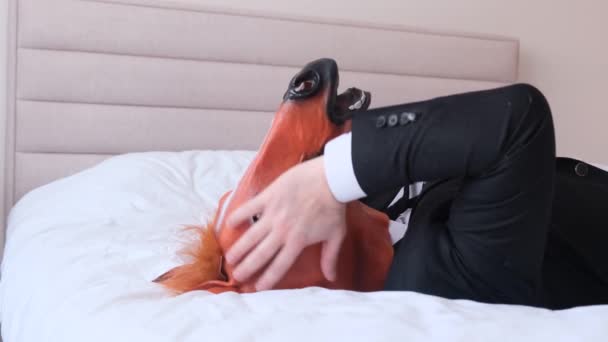 馬の頭を持つビジネスマンがベッドで休んでいる 彼は頭痛を持っています 疲れたサラリーマン 4Kビデオ — ストック動画