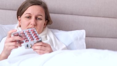 A young woman is lying in bed, she is sick and will drink pills for a cold. Treatment of influenza virus.