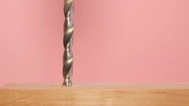 On a pink background, a drill while drilling wood, close-up. A shiny metal drill bit at work. Slow motion