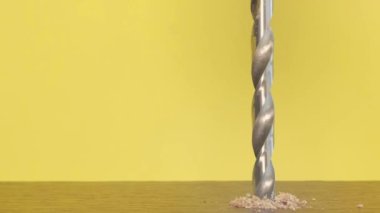 Close-up of a woodworking drill rotating on a yellow background. A shiny metal drill bit at work. Slow motion