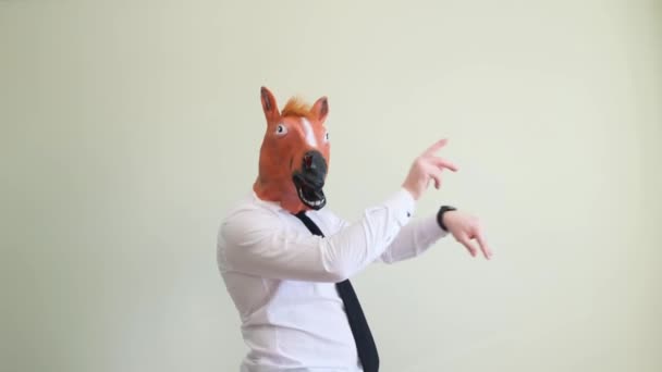 奇妙なカーニバルの馬のマスクの面白い男が踊っていて スタジオで軽い背景で楽しんでいます 馬仮面舞踏会の仮面 — ストック動画