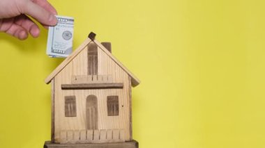 Adamın biri, sarı arka plandaki kumbaraya para yatırıyor. Konut satın almak, ev finansmanı için para biriktirmek.