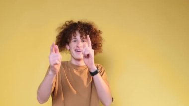 A cheerful, playful young man with a chic hairstyle shows positive emotions to the camera. Hand gestures. A student on a brown background