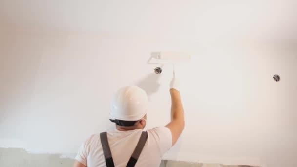 公寓的现代化改造 一个穿着特殊制服的男人用滚子在公寓里画墙壁 墙是白的 — 图库视频影像