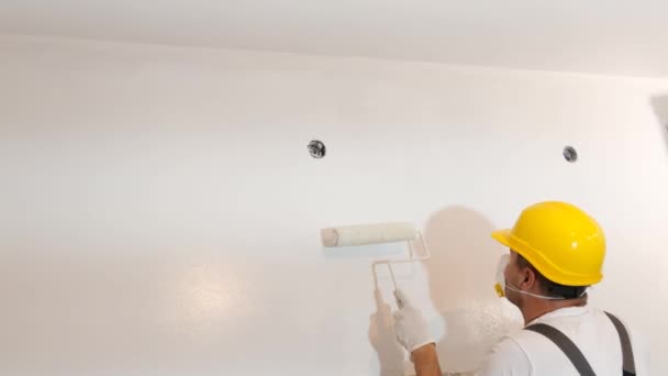 一位身穿制服 头戴黄色硬礼帽的年轻主人把墙壁漆成了明亮的白色 新公寓的翻修 — 图库视频影像