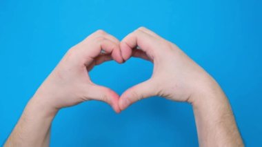 A view of a male hand making a heart-shaped gesture, isolated on a blue screen chromakey background. A person forms a heart with the help of fingers. Gestures with two hands. Close up