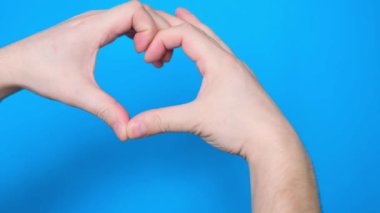Close-up of a mans hand making a heart-shaped gesture, isolated on a blue screen chromakey background. A person forms a heart with the help of fingers. Close up