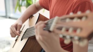 Close up of young guy playing guitar in his room. He is sitting on the couch and passionately enjoying the music. 4k video