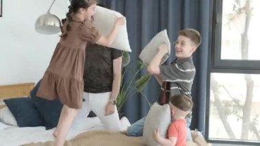 Gülümseyen aile yatak odalarında yastıklarla eğleniyor, kahkaha ve gülümseme dolu..