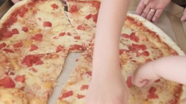 Karton bir kutudan bir dilim pizza alan bir ailenin yakın çekimi. Çocuklar ve ailelerin pizza yediği en iyi manzara. Pizza teslimatı