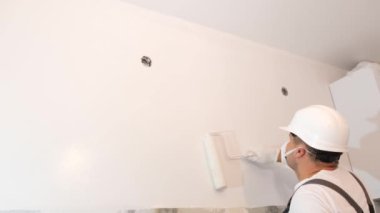 A repairman in a mask and helmet paints the wall white. Modern renovation in the apartment