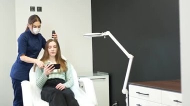 Consultation of a trichologist. A doctor diagnoses a young girls hair structure using a smartphone. Technologies in medicine