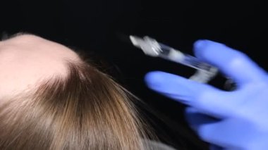 A trichologist in medical gloves gives a woman an injection against hair loss. Treatment of diseases of the scalp