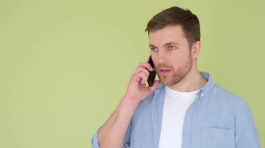 Aggressive man talking on smartphone and shouting displeased, isolated on background in studio. A guy with a nervous breakdown