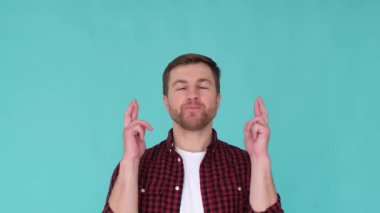 Caucasian young man in casual clothes crossing fingers for happiness on background in studio. He has an expectant look on his face, like hes expecting something good to happen.