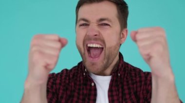 Portrait of a man who feels the satisfaction of victory, raises his hands up and shouts something. Happy facial expression of a young man.