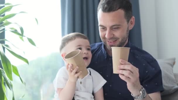 笑顔のお父さんは彼の腕の中で彼の小さな息子を保持し 使い捨てメガネから水を飲む 4Kビデオ — ストック動画