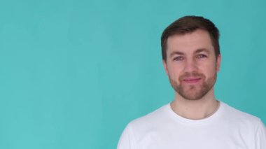 Handsome young man smiling at camera and giving thumbs up on blue background. The concept of winner, success, winning