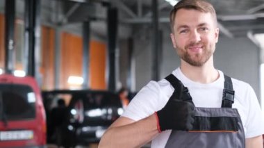 Otomobil tamircisinin portresi kameraya bakıp gülümsüyor. Arabaların profesyonel onarımı ve bakımı.