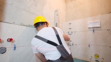 Profesyonel bir zanaatkar bir kat ve cetvel kullanarak banyo duvarına fayanslar serer. Modern bir iç mekanı olan bir tuvalet yaratmak.