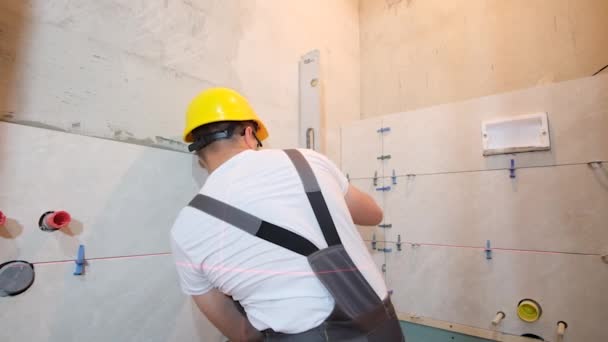 一个专业的工匠用一个水平仪和一把尺子把瓷砖铺在浴室的墙上 创建一个现代化的室内浴室 — 图库视频影像