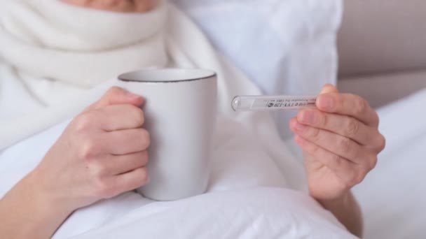 白いお茶のカップを保持し 温度計で温度を測定病気の女性のクローズアップ 自宅でのSarsの治療 — ストック動画