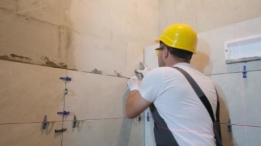 Male professional master laying ceramic tiles on wall in bathroom. Portrait of an experienced repairman man placing a large size tile.