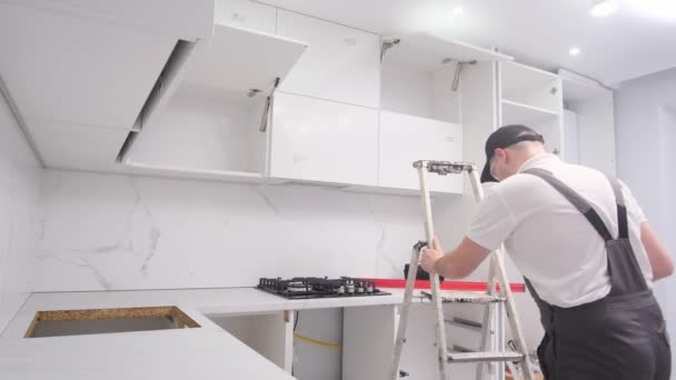 Worker Assembles Modern Kitchen Furniture Using Ladder Installation Kitchen Cabinets — Stock video