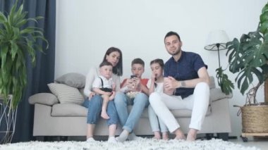 Happy family spending time together at home. They watch a movie, hug and eat popcorn. The family members look satisfied with the time spent together