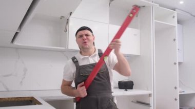 Funny and fun kitchen furniture assembler simulates playing the guitar with a construction level. Happy young worker of European appearance at work