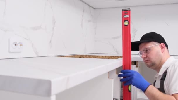 一位穿着工作服的专业建筑商在工具的帮助下 检查了一个平面厨房柜的质量水平 新公寓的修理工作 — 图库视频影像